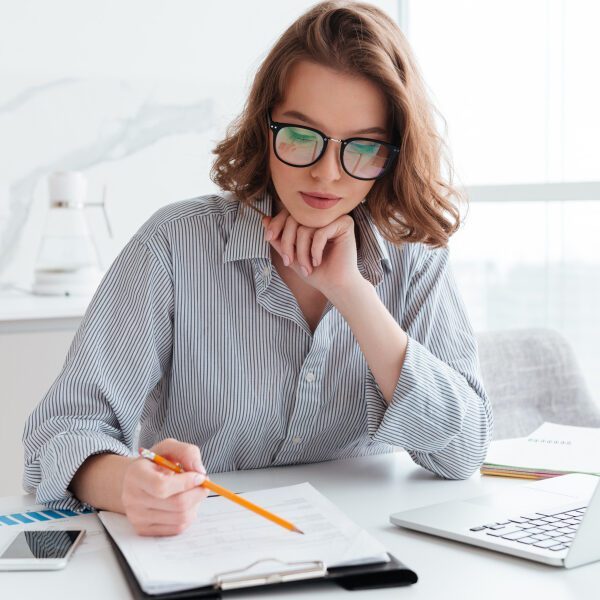 young-concentrated-businesswoman-in-glasses-and-striped-shirt-working-with-papers-at-home